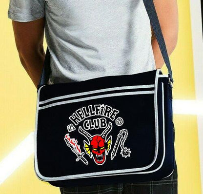 A black Hellfire stranger things style messenger bag with an adjustable shoulder strap and a front flap closure. The bag features a red and yellow graphic on the front and is made of polyester.