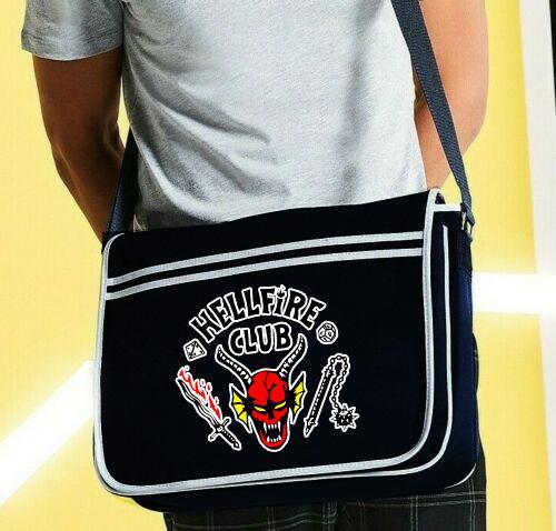 A black Hellfire stranger things style messenger bag with an adjustable shoulder strap and a front flap closure. The bag features a red and yellow graphic on the front and is made of polyester.