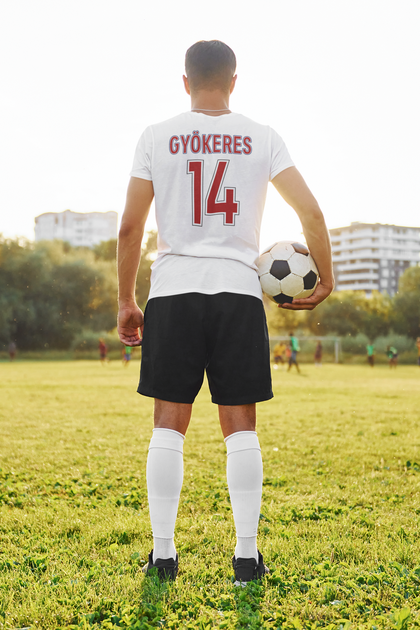 Soccer player holding a ball on a field with buildings in the background