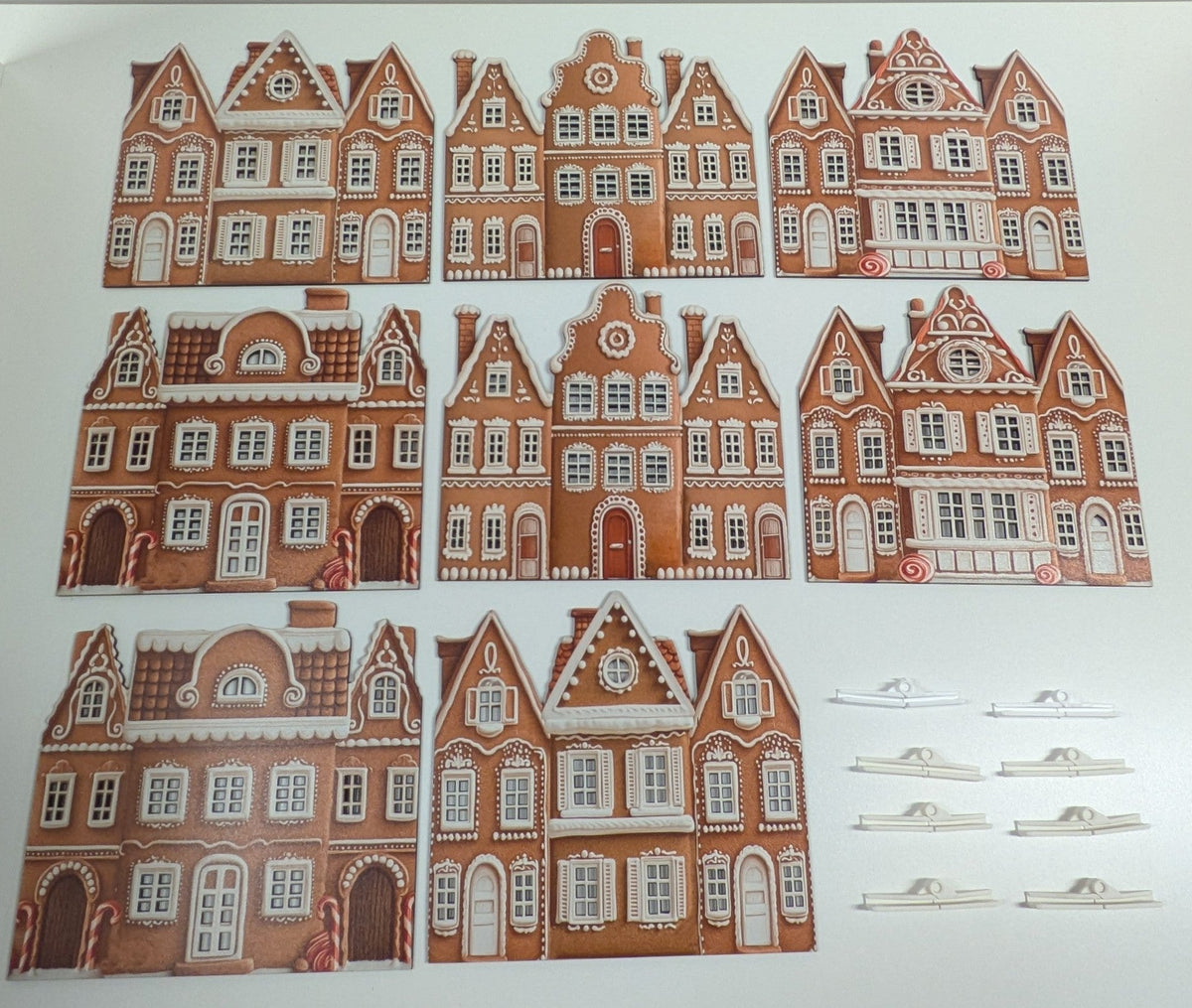 A set of traditional Dutch gingerbread house templates or cut-out pieces arranged on a white background, including several larger house designs and six small white tabs or connectors.