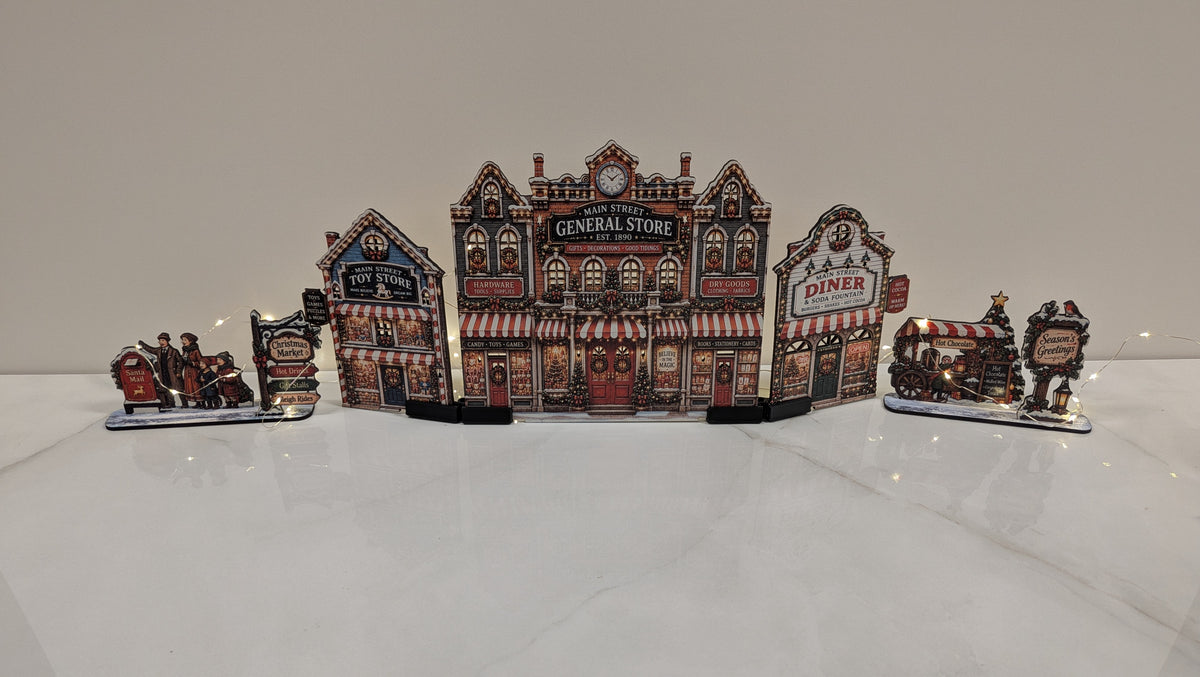 A decorative miniature village scene with a central General Store building and adjacent diner and train carriages, displayed on a glossy white surface against a plain light background.