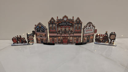 A decorative miniature village scene with a central General Store building and adjacent diner and train carriages, displayed on a glossy white surface against a plain light background.