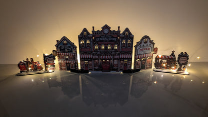 A miniature diorama set featuring a central vintage general store with glowing windows, flanked by a diner, a small train car, and decorative street signs, displayed on a reflective surface against a warm gradient background.